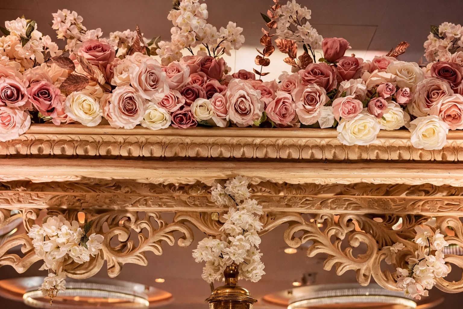 Close detail of a hand-carved mandap canopy crowned with blush, dusky pink and ivory roses and trailing white blossom